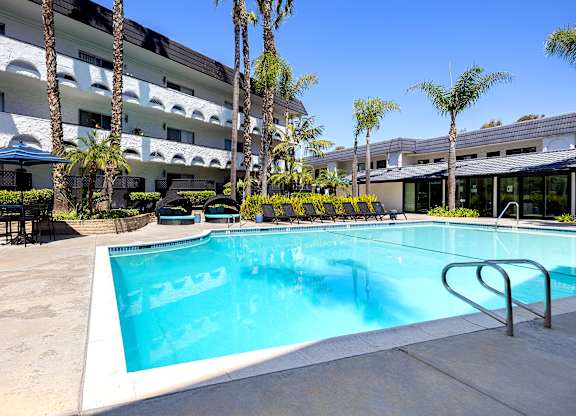 A swimming pool in front of a building with palm trees.