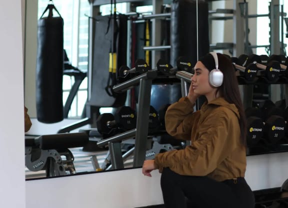 a woman sitting on a bench in a gym with headphones on