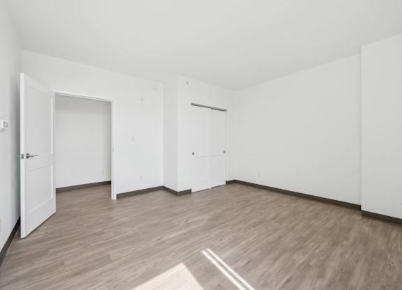 A room with white walls and wooden flooring with a rug in the middle.