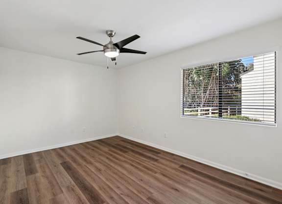 A room with a ceiling fan and a window with blinds.