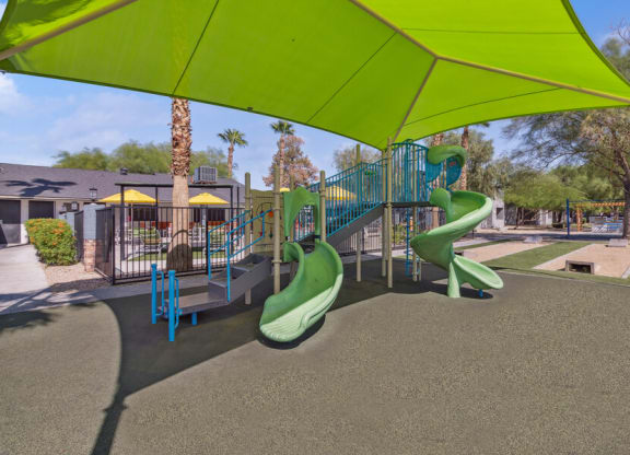 a playground with slides and a swing set under a green canopy