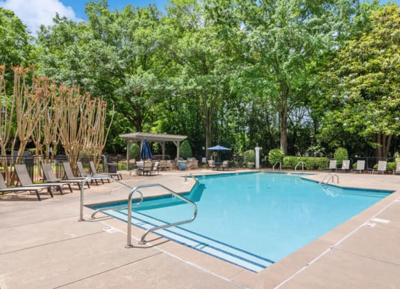 a swimming pool with chaise lounge chairs and trees in the background