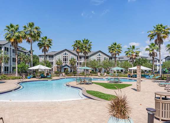 A swimming pool surrounded by palm trees and a resort-style building.