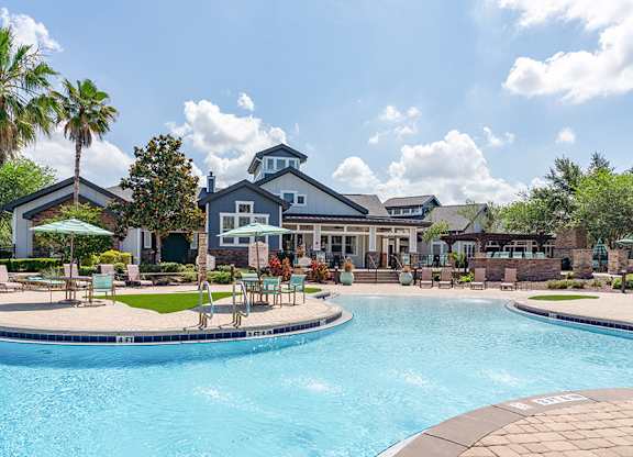 A swimming pool in front of a house with a patio and chairs.