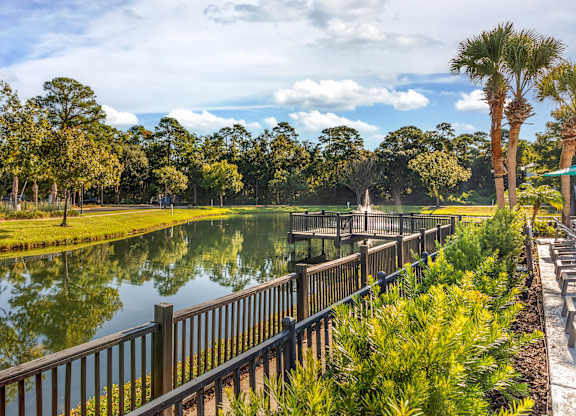 A serene park with a lake, trees, and a wooden fence.