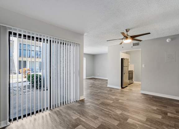 Model living room with ceiling fan, sliding door to patio, and wood flooring at Oasis at Bayside in Largo, FL.