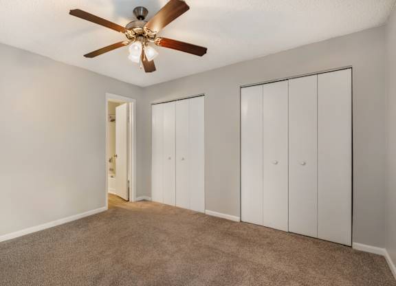 A room with a ceiling fan and three white doors.
