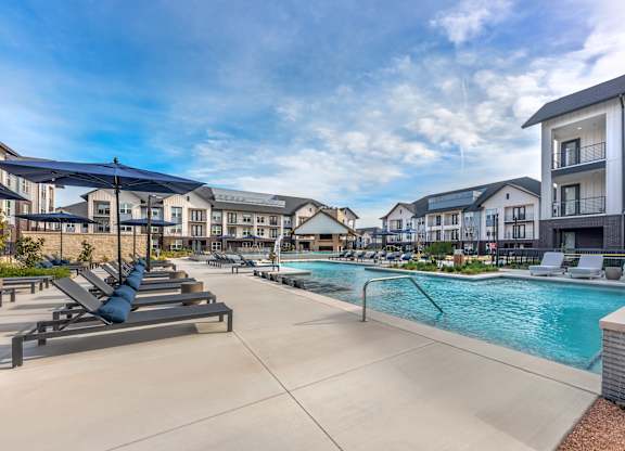 A swimming pool surrounded by sun loungers and umbrellas in a residential area.