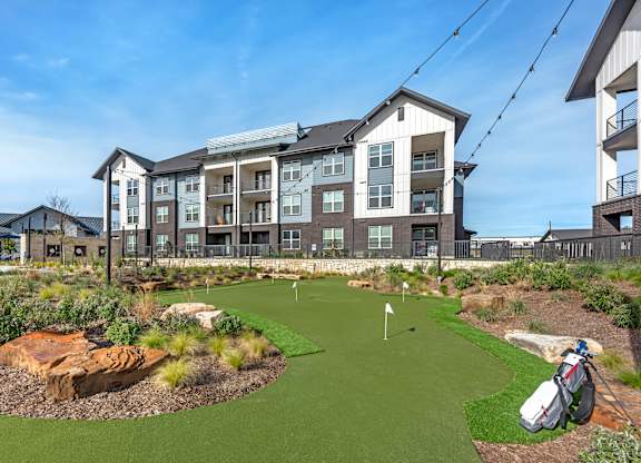 A golf hole is in the front yard of a large apartment complex.