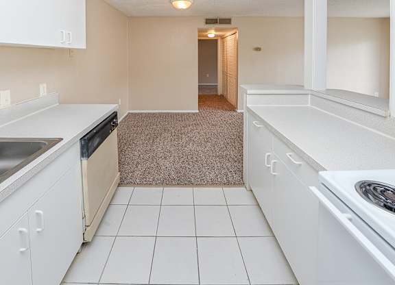 A kitchen with white cabinets and a beige carpet.