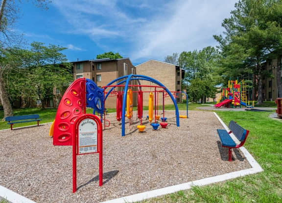 Apartments in Silver Spring, MD - Spring Parc - Colorful Playground With Climbing Structures, Swings, Benches, And Nearby Apartment Buildings Framed By Trees And Green Lawn