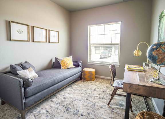 A living room with a grey sofa, a wooden table, a chair, a globe, and a window.