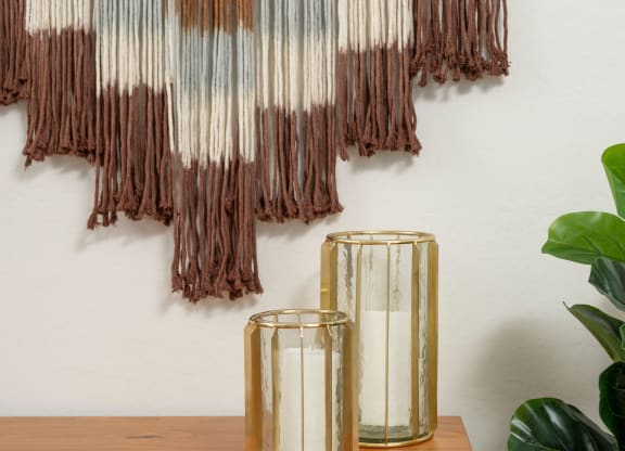 a piece of artwork hangs on a wall next to a table with two candles and a plant