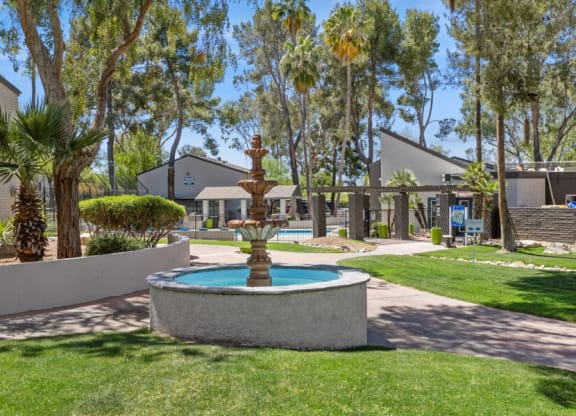 a fountain in the middle of a grassy area with apartments in the background