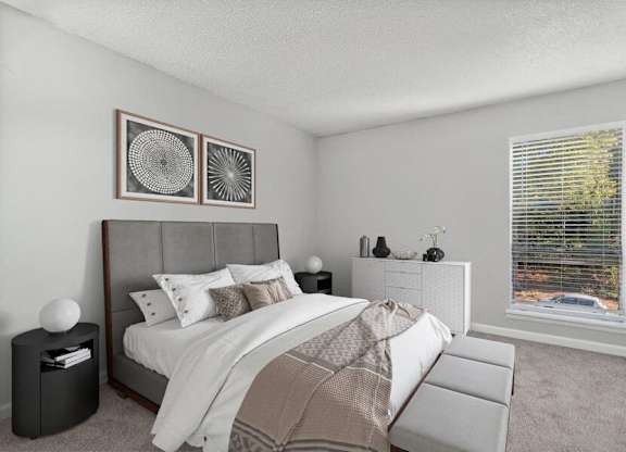 One-Bedroom Apartments in Raleigh, NC - Bridges at North Hills - A Bedroom With Carpet Flooring, A Large Bed, Matching Nightstands, Framed Wall Art, A Dresser, And A Large Window.