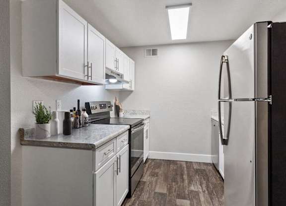 Dog-Friendly Apartments in Federal Way, WA - Sunset Three Twenty - A Kitchen With White Cabinets, Gray Countertops, Stainless Steel Refrigerator, And Stove.