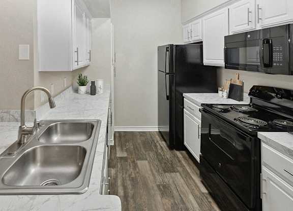 Dog-Friendly Apartments in Garland, TX - The Belmont at Duck Creek - A Kitchen With White Cabinets, Marble Look Countertops, Double Stainless Steel Sink, And Microwave.