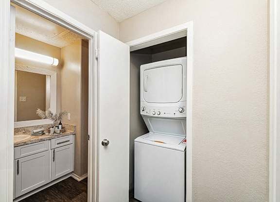 Luxury Apartments in North Dallas, TX, with In-Unit Washer and Dryer - Dallas North Park - A Laundry Area With A Closet Beside Bathroom Vanity With Mirror, Lighting, And Countertop.