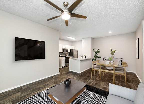 Dog-Friendly Luxury apartments in North Dallas, TX - Dallas North Park - Living Room With Ceiling Fan, Wall-Mounted Television, Coffee Table, and Kitchen Breakfast Bar.