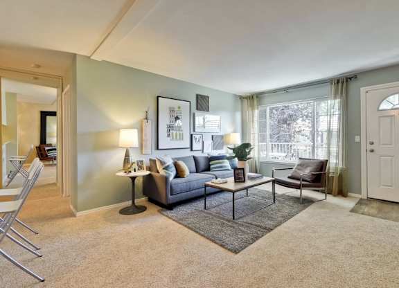 A living room with a grey couch, a black and white picture frame, a grey rug, a black floor lamp, a white door, a white wall, a white ceiling, a white chair, a white table, a white floor lamp