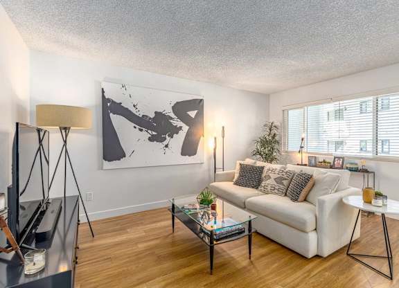 A living room with a white couch, a coffee table, and a large abstract painting on the wall.