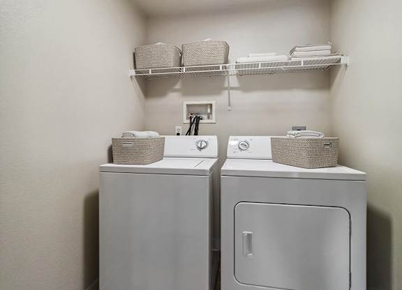 A small laundry room with two washing machines and a shelf above them.