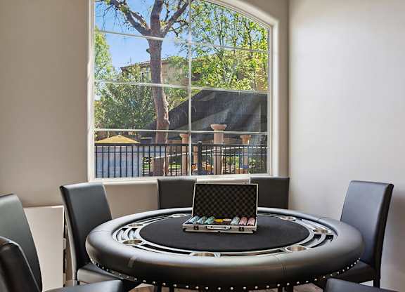 A poker table is set up in a room with a view of a tree outside the window.