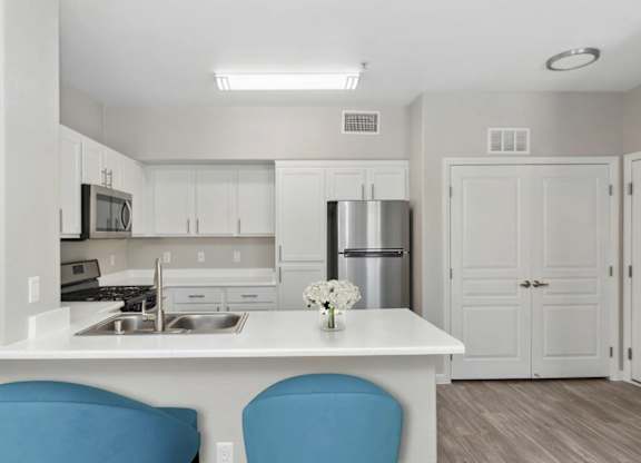 A kitchen with white cabinets and a white island with blue chairs.