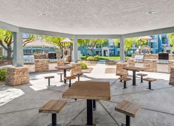 A patio with tables and benches is surrounded by a white wall.