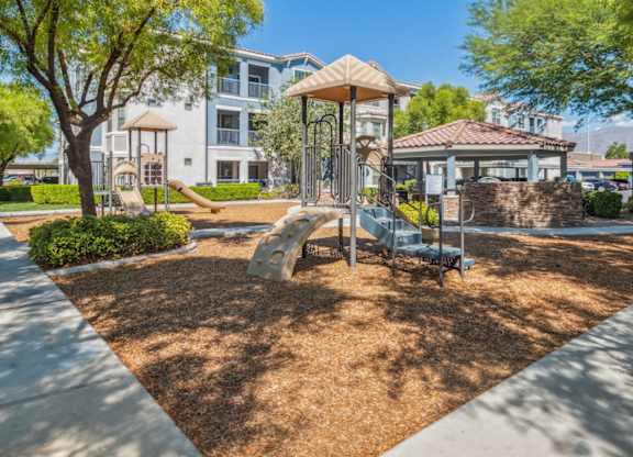 A playground with a swing set and a slide in the foreground and apartment buildings in the background.