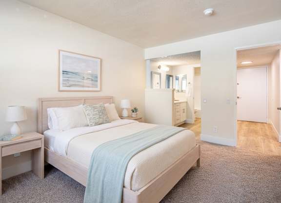 A bedroom with a bed, nightstand, and a painting on the wall.