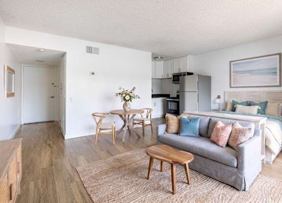 A living room with a grey couch, a wooden coffee table, and a dining table with chairs.