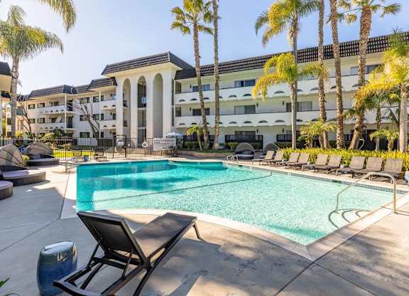 A pool surrounded by palm trees and lounge chairs.