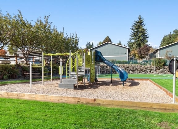 Playground in boxed in area full of sand surrouned by lush green landscape