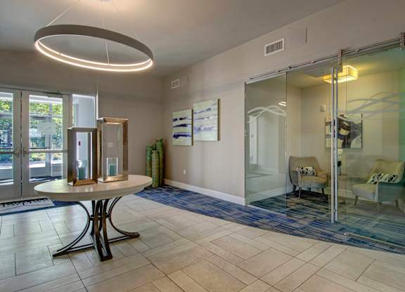 A white table with a black base is in the middle of a room with a glass wall and a mirror.