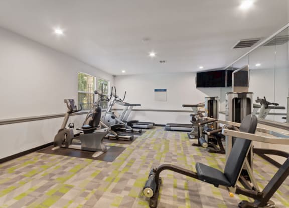 Federal Way, WA, Apartments Near Walmart - Sunset Three Twenty - A Fitness Center With Cardio Machines, Weight Equipment, Wall Mirrors, And Mounted Television Screens.
