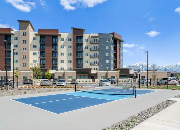 A tennis court in front of a multi-story apartment building.