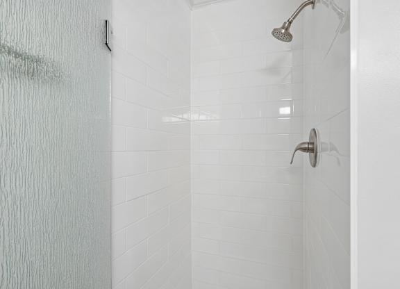 A white tiled shower with a shower head and hand held shower.