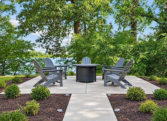 A concrete patio with a table and chairs surrounded by greenery.