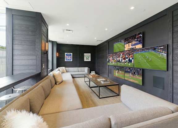 A modern living room with a large couch and a TV displaying a soccer game.