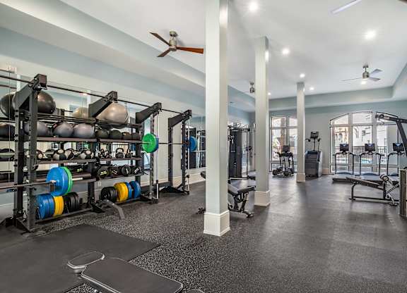 A gym with a variety of equipment including weight plates, weightlifting equipment, and a bench press at The Addison, Baton Rouge, Louisiana