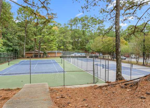 A tennis court surrounded by trees and a fence. at Riverchase Landing Apartments, Hoover, AL