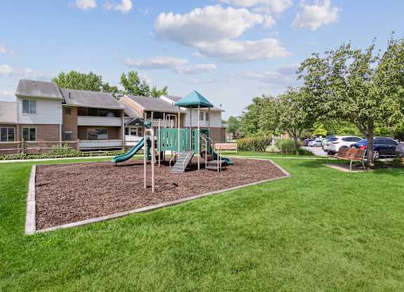 A playground with a green slide and a wooden swing set.