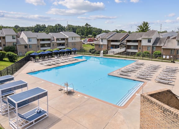 A swimming pool surrounded by sun loungers and apartment buildings.