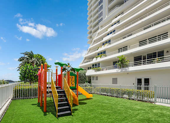 Outdoor childrens playground with colorful equipment and artificial turf at The Hamilton Apartments, Miami, FL 33137
