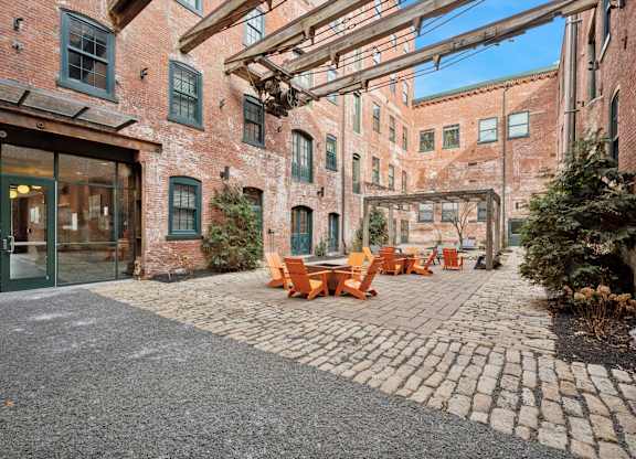 A courtyard with a cobblestone floor and orange chairs.