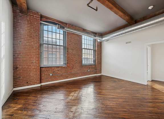 A room with wooden floors and a brick wall with a window.