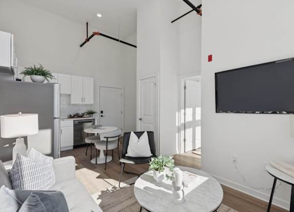 A modern living room with a grey sofa, a white coffee table, and a black television mounted on the wall.