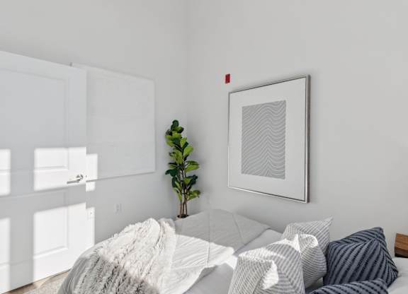 A bedroom with a bed covered in a white blanket and a framed picture on the wall.