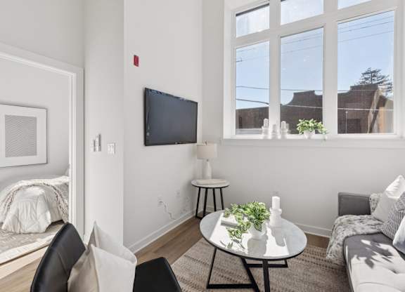 A living room with a grey couch, a black chair, a white coffee table, and a flat screen TV mounted on the wall.